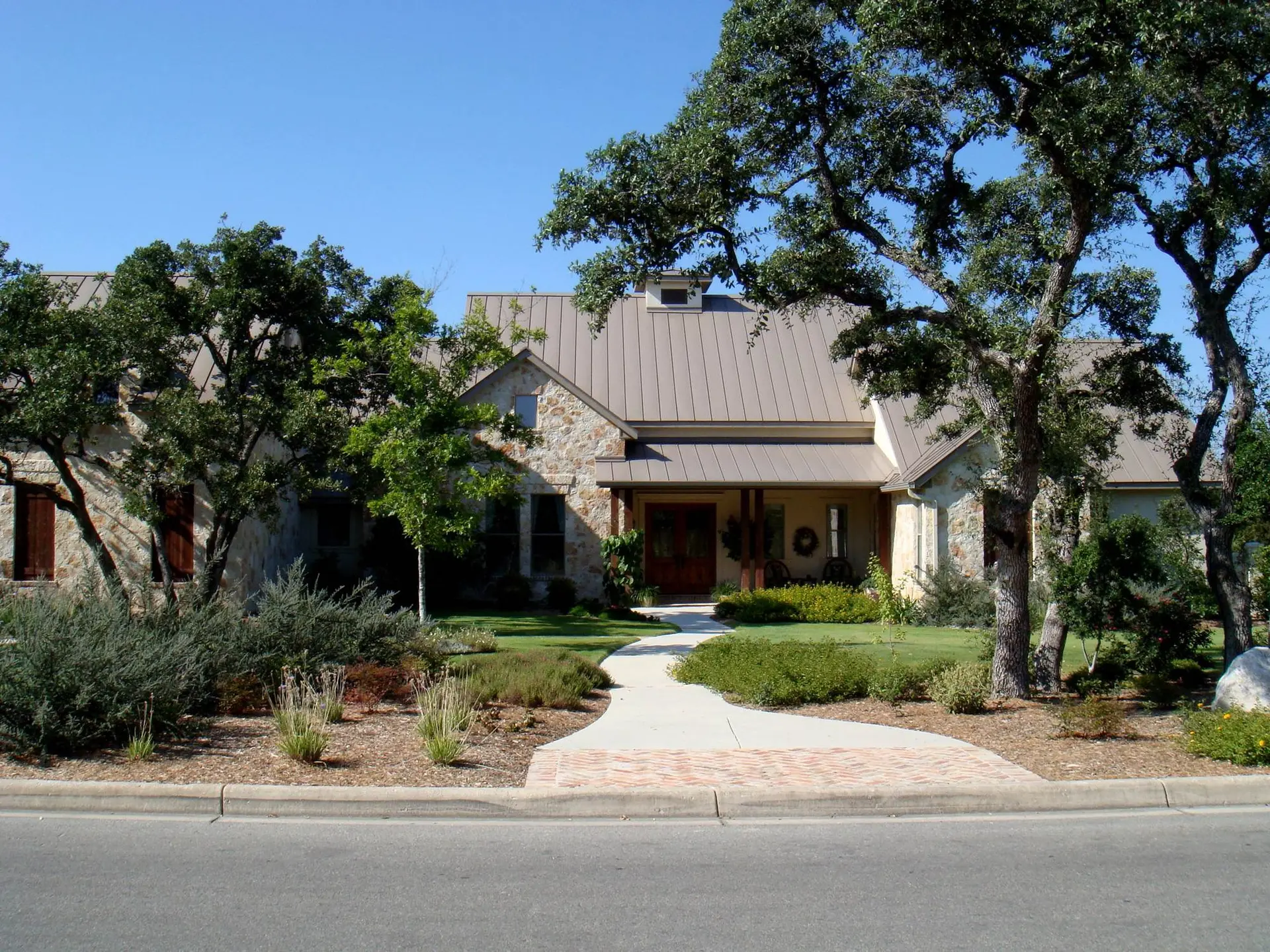 A landscaped San Antonio property with a green lawn, planted borders, and mature oak trees